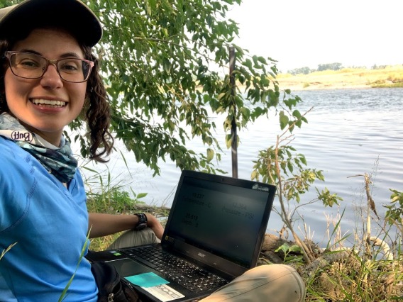 Christina Morrisett with her laptop next to a lake.