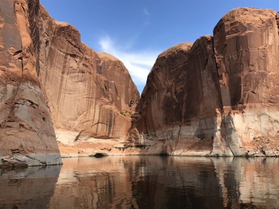 Lave Powell viewed from the water with tall canyon walls in the distance.