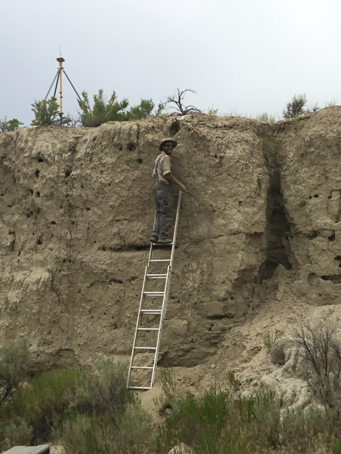 John Kemper standing on a ladder leaning on a cliffside looking back with a smile.