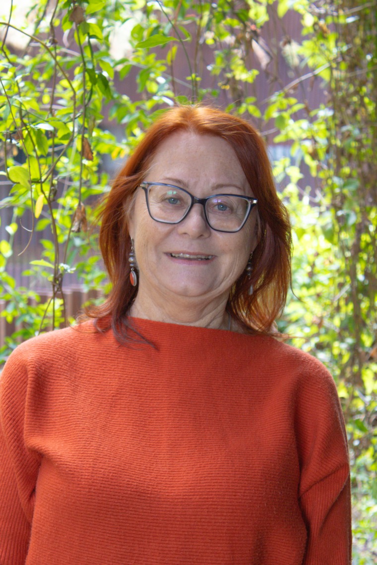 Anita Govert in front of foliage, wearing an orange sweater