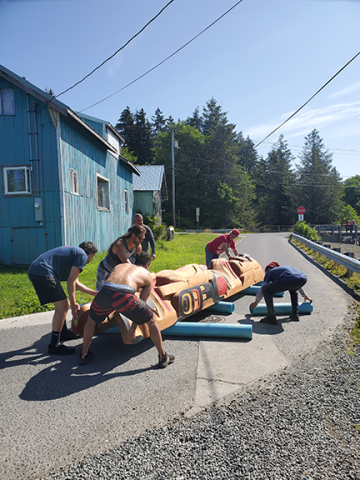A group of people moving a large object on rollers down a small street.
