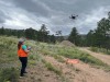 Lauren wearing an orange sweater looking up at a drone airborne with trees and clouds in the background